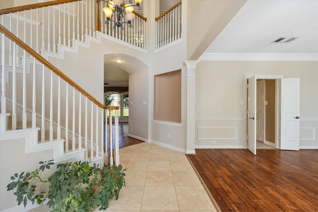 entryway featuring ornamental molding, a chandelier, light wood-type flooring, and decorative columns