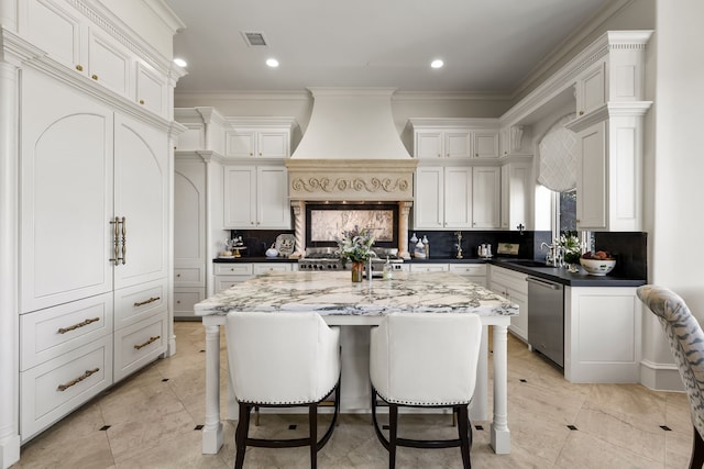 kitchen featuring light stone countertops, an island with sink, backsplash, stainless steel appliances, and custom range hood