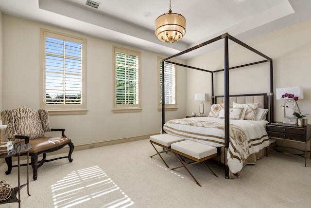 bedroom featuring light carpet, a raised ceiling, and a chandelier