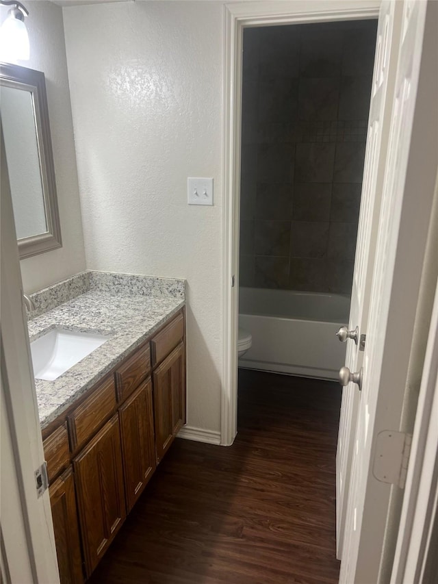 bathroom featuring toilet, a textured wall, wood finished floors, and vanity