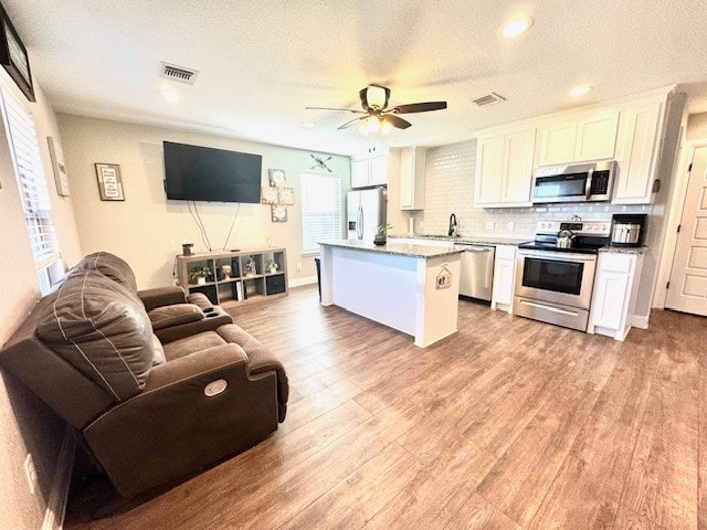 kitchen with appliances with stainless steel finishes, a center island, white cabinetry, ceiling fan, and light hardwood / wood-style flooring