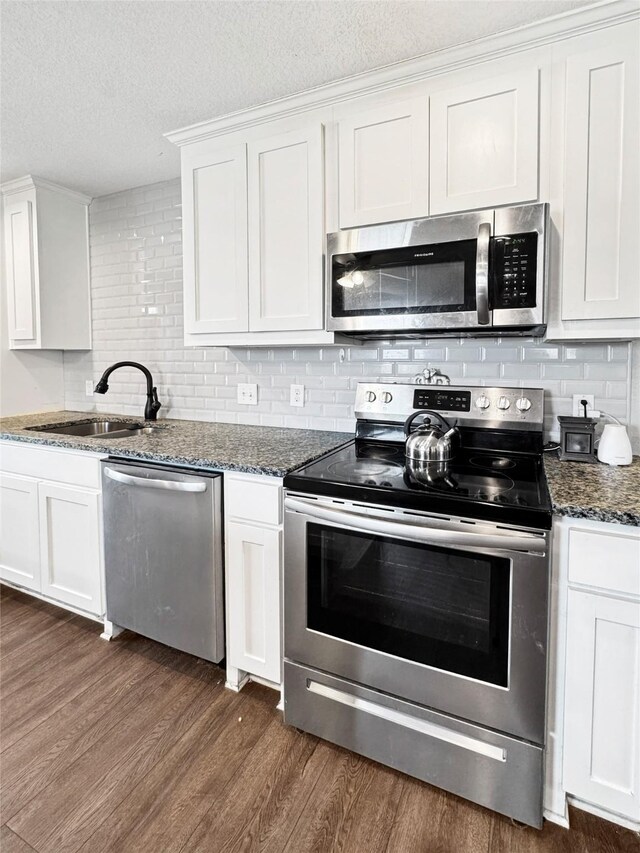 kitchen with dark wood-type flooring, sink, light stone countertops, white cabinetry, and appliances with stainless steel finishes