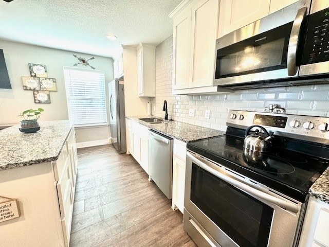 kitchen featuring white cabinetry, stainless steel appliances, light stone countertops, and sink