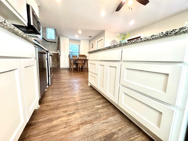 kitchen featuring dark wood-type flooring, dark stone countertops, white cabinetry, appliances with stainless steel finishes, and ceiling fan