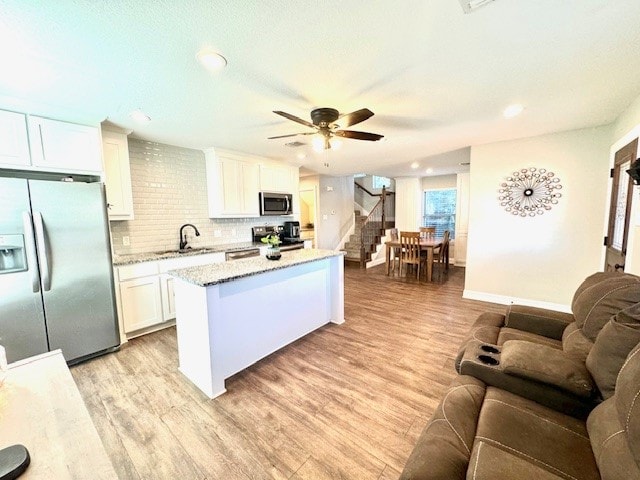 kitchen with light hardwood / wood-style flooring, light stone countertops, a center island, white cabinets, and appliances with stainless steel finishes