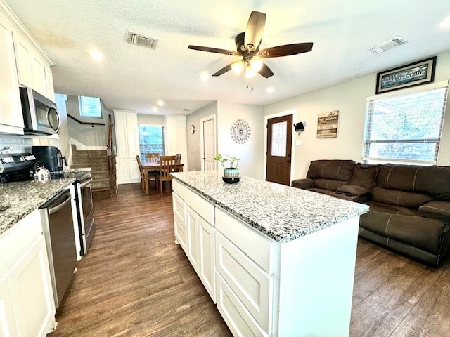 kitchen featuring white cabinets, a kitchen island, appliances with stainless steel finishes, light stone countertops, and dark hardwood / wood-style floors