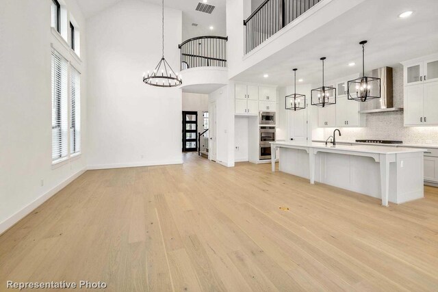 kitchen with a center island with sink, hanging light fixtures, a towering ceiling, and range hood