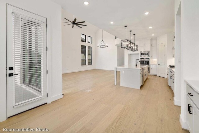 kitchen with stainless steel microwave, an island with sink, hanging light fixtures, white cabinetry, and light hardwood / wood-style flooring