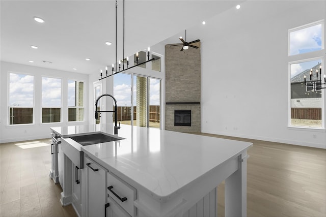 kitchen with a fireplace, wood finished floors, open floor plan, an island with sink, and pendant lighting