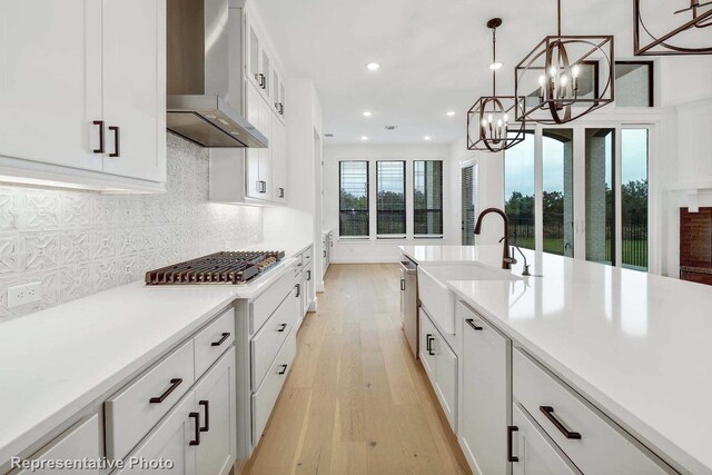 kitchen with wall chimney exhaust hood, light hardwood / wood-style flooring, stainless steel gas cooktop, and white cabinetry