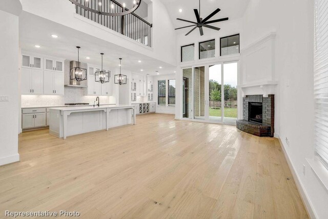 unfurnished living room featuring a towering ceiling, sink, ceiling fan with notable chandelier, a brick fireplace, and light hardwood / wood-style flooring