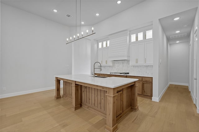 kitchen featuring pendant lighting, a large island with sink, white cabinets, sink, and backsplash