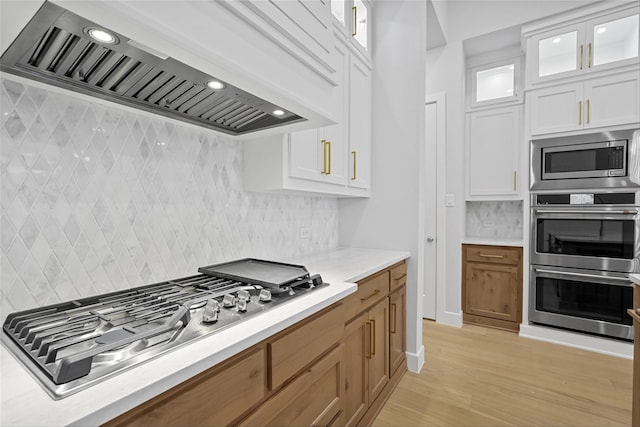 kitchen with light hardwood / wood-style flooring, appliances with stainless steel finishes, wall chimney exhaust hood, backsplash, and white cabinets