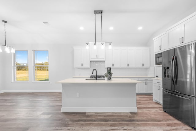 kitchen with stainless steel fridge with ice dispenser, vaulted ceiling, decorative light fixtures, a kitchen island with sink, and white cabinets