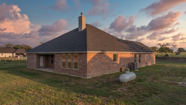 back house at dusk featuring central AC unit, a patio area, and a lawn