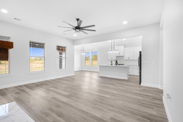 unfurnished living room featuring light wood-type flooring, ceiling fan with notable chandelier, and sink