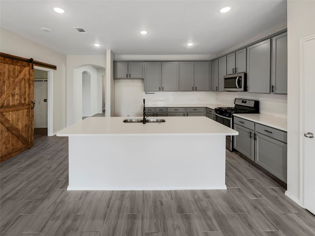 kitchen with an island with sink, gray cabinetry, stainless steel appliances, sink, and a barn door