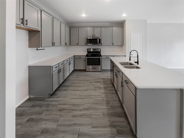 kitchen with appliances with stainless steel finishes, sink, a center island with sink, and gray cabinets