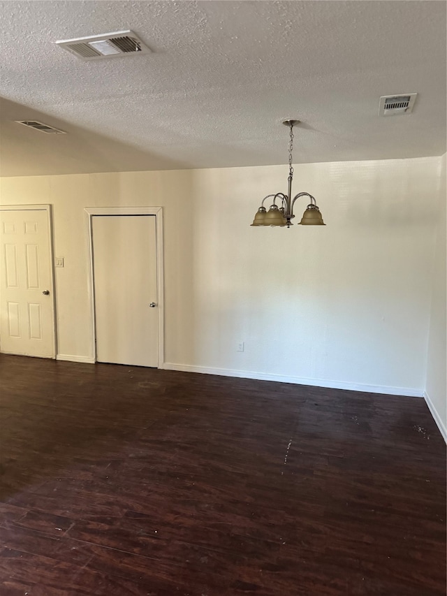 empty room featuring a textured ceiling, a chandelier, and dark hardwood / wood-style flooring