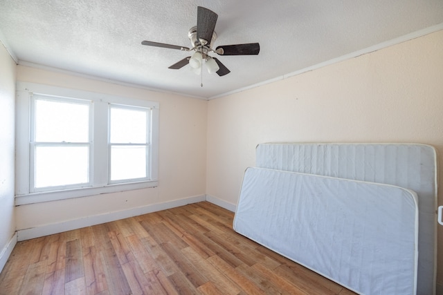 unfurnished bedroom with ceiling fan, a textured ceiling, ornamental molding, and light hardwood / wood-style flooring