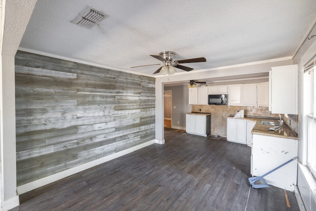 kitchen with sink, a textured ceiling, dark hardwood / wood-style flooring, white cabinetry, and wooden walls