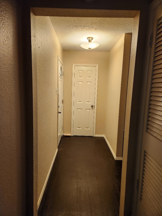 corridor featuring baseboards, a textured wall, dark wood-style floors, and a textured ceiling