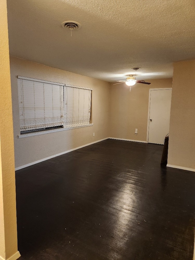 empty room featuring dark wood-type flooring, ceiling fan, and a textured ceiling