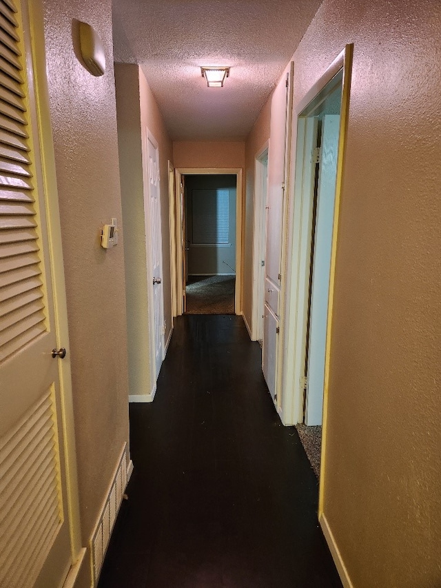 hallway with baseboards, a textured wall, a textured ceiling, and visible vents