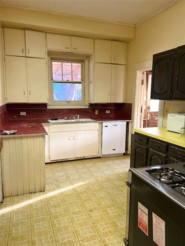 kitchen with white dishwasher, a sink, cream cabinetry, and stove