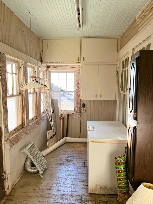 clothes washing area with wood walls, a wealth of natural light, cabinet space, and wood-type flooring