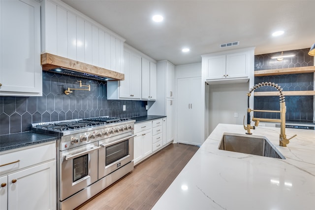 kitchen with white cabinetry, dark stone counters, and range with two ovens