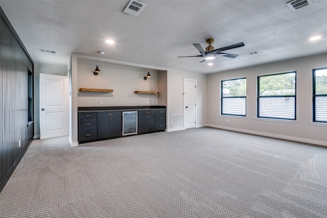 unfurnished living room with wine cooler, a textured ceiling, light colored carpet, and ceiling fan