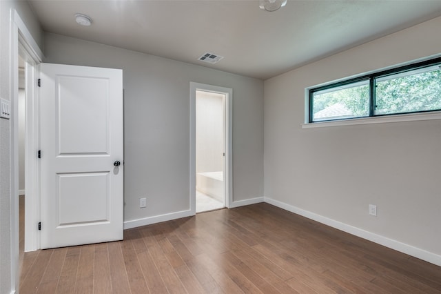 unfurnished bedroom featuring hardwood / wood-style floors and connected bathroom