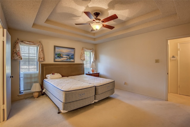 carpeted bedroom featuring a textured ceiling, ceiling fan, multiple windows, and a raised ceiling