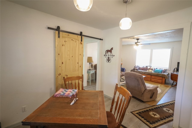 dining space with ceiling fan, a barn door, and hardwood / wood-style floors