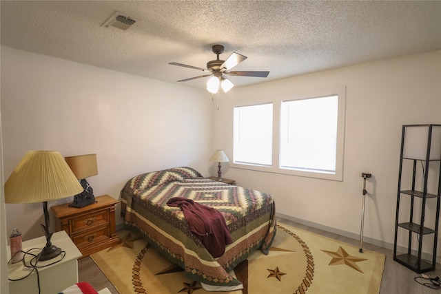 bedroom with light hardwood / wood-style flooring, a textured ceiling, and ceiling fan