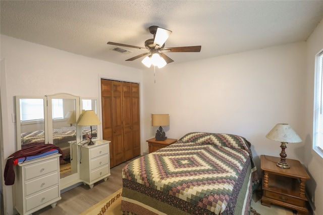 bedroom with light hardwood / wood-style flooring, a textured ceiling, a closet, and ceiling fan