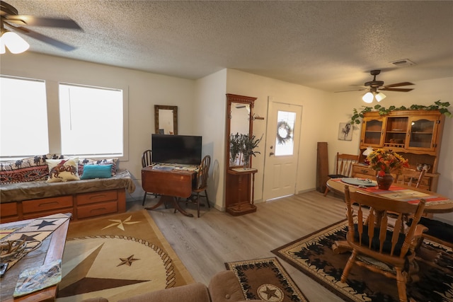 living room featuring a textured ceiling, light wood-type flooring, and ceiling fan