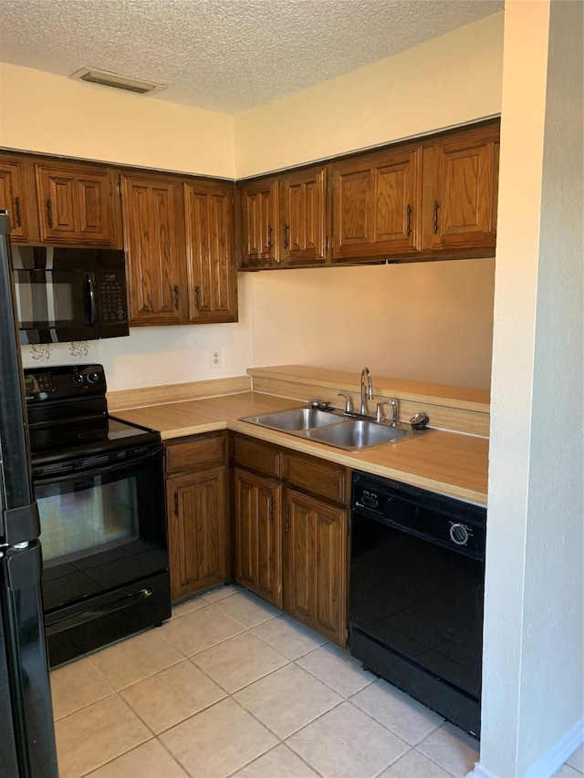 kitchen with a textured ceiling, black appliances, sink, and light tile patterned floors