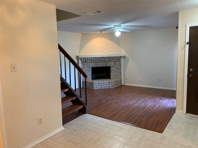 unfurnished living room with light hardwood / wood-style floors, a textured ceiling, a fireplace, and ceiling fan