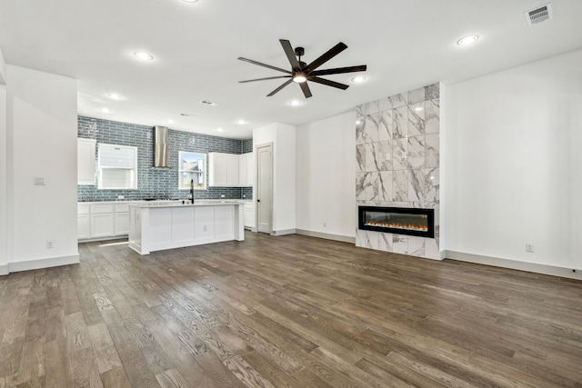 unfurnished living room with sink, ceiling fan, a fireplace, and dark hardwood / wood-style flooring