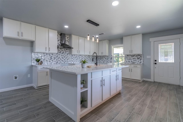 kitchen with wall chimney range hood, wood-type flooring, pendant lighting, a center island with sink, and white cabinetry