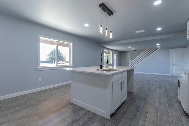 kitchen with white cabinets, dark hardwood / wood-style flooring, a kitchen island with sink, and sink