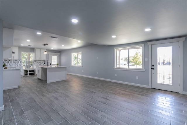 kitchen with white cabinetry, hanging light fixtures, dark wood-type flooring, tasteful backsplash, and an island with sink