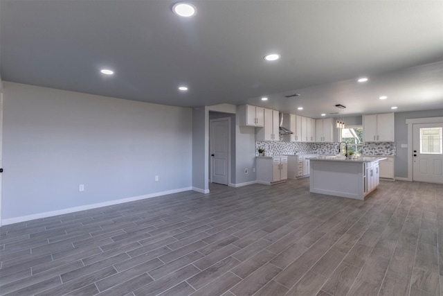 kitchen featuring dark hardwood / wood-style flooring, wall chimney range hood, pendant lighting, a center island, and white cabinetry