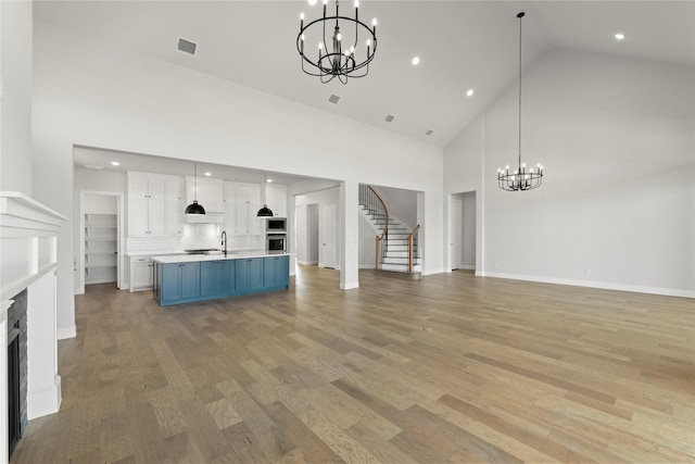 unfurnished living room featuring visible vents, stairway, light wood-style floors, a fireplace, and a chandelier