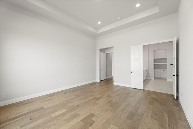 unfurnished bedroom with baseboards, a raised ceiling, a towering ceiling, light wood-type flooring, and recessed lighting