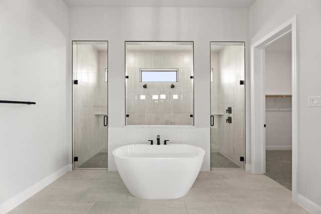 bathroom featuring a walk in closet, a soaking tub, a stall shower, tile patterned flooring, and baseboards