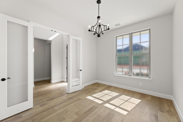 empty room with french doors, light wood finished floors, visible vents, a chandelier, and baseboards