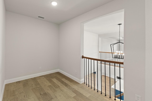 corridor featuring baseboards, wood finished floors, visible vents, and an inviting chandelier